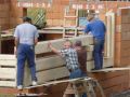 V areálu vznikají další roubenky. Po dokončené zděné části stavby zedníky, nastupují se dřevem zkušení tesaři. 