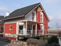 Rodinný dům s červenou fasádou postavený nad vodou.